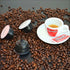 Eine Tasse Quaranta Caffè in einer Szenerie mit Kaffeebohnen und Nescafè Dolce Gusto Kapseln
