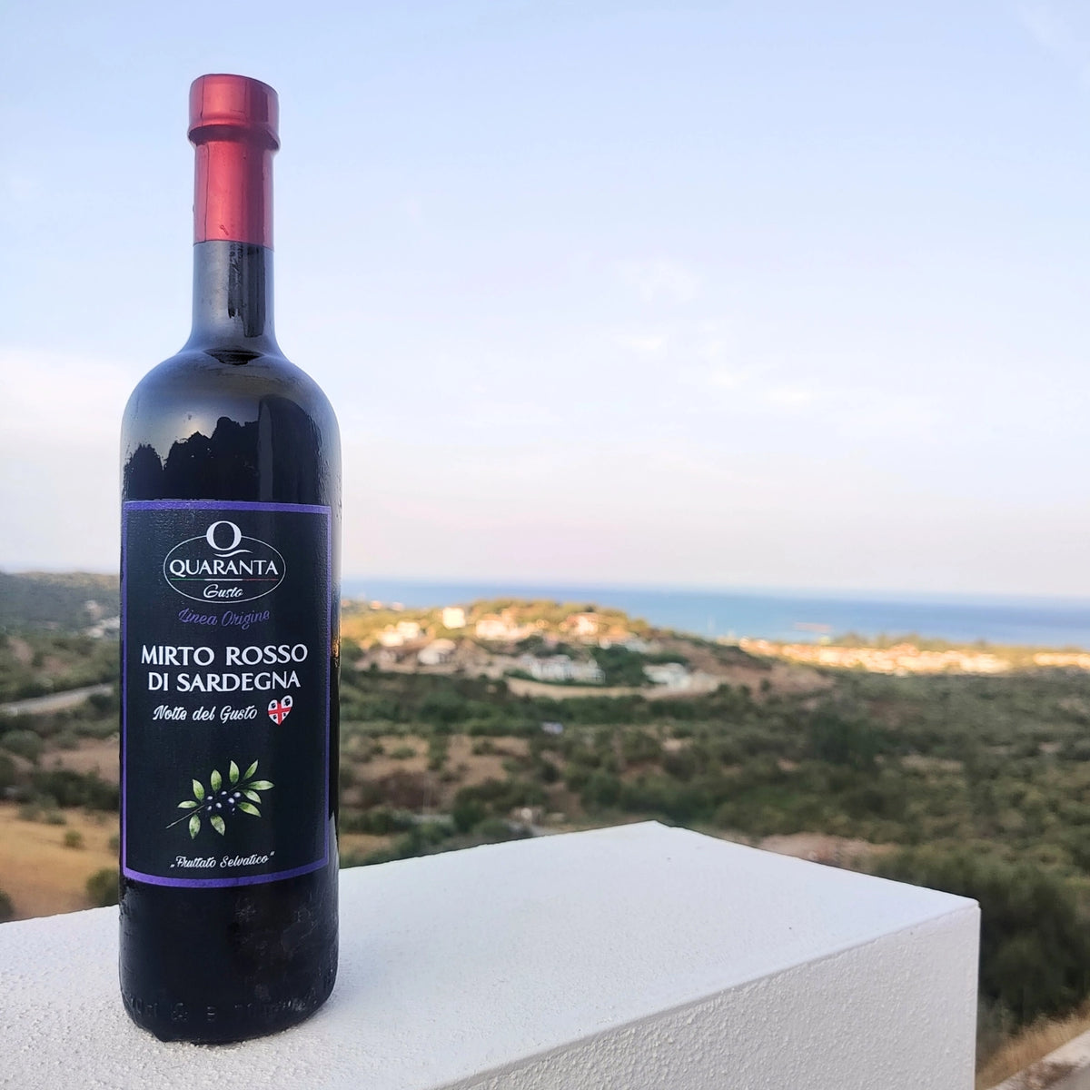 Quaranta Gusto Mirto-Likör-Flasche auf Sardinien bei Sonnenuntergang; im Hintergrund die Costa Smeralda.